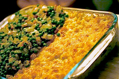 Casserole dish with macaroni and cheese, half topped with peas and bacon.