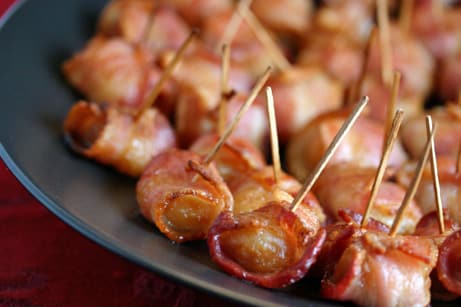 Bacon-wrapped water chestnuts with toothpicks holding them closed on a plate.