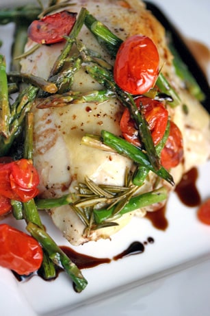 Roasted chicken breast with asparagus and tomatoes on a plate.