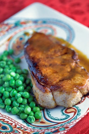 Pork chop with bourbon glaze and peas on a plate.