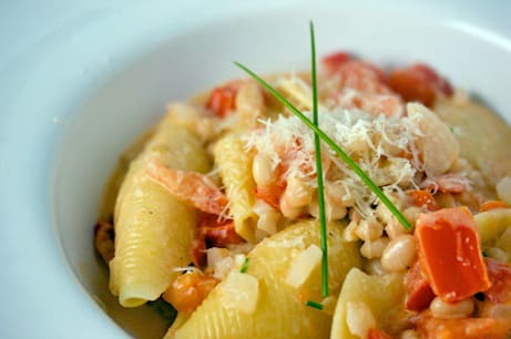 Bowl of pasta shells with beans and tomatoes.