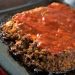 Meatloaf topped with ketchup on a baking sheet.