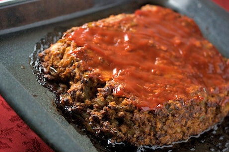 Meatloaf topped with ketchup on a baking sheet.