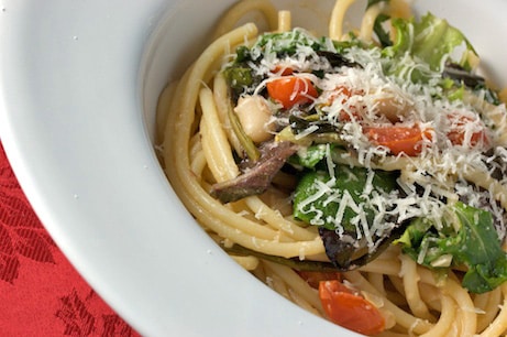 A bowl of pasta with greens and tomatoes.