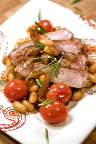 Sliced steak with white beans and tomatoes.