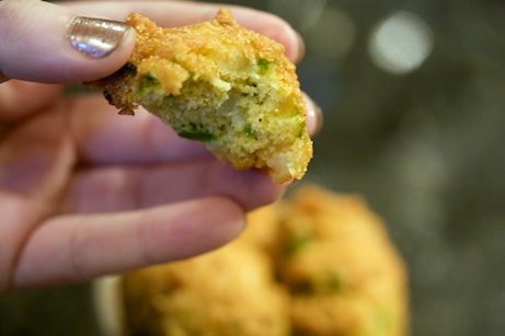 Hand holding a hush puppy with a bite taken out of it.