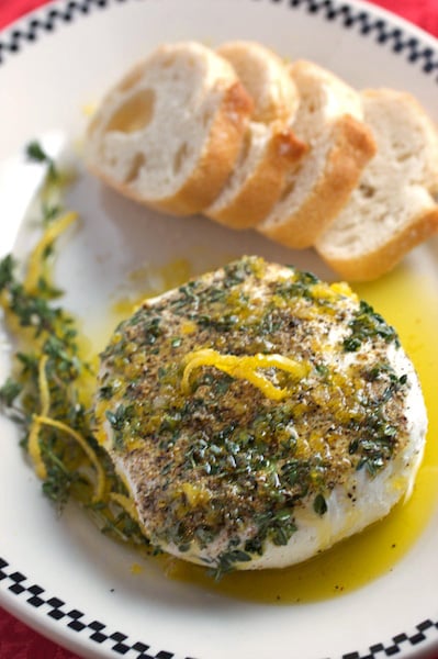 Plate of goat cheese with herbs and lemon with bread alongside.