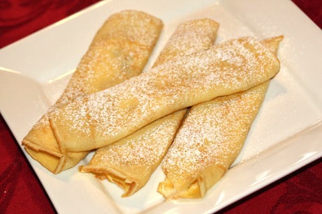 Pile of rolled crepes dusted with powdered sugar.