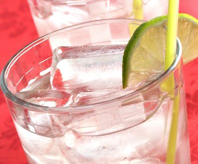 Two glasses of gin and tonics garnished with lime wedges.