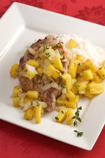 A pork chop with pineapple relish and rice.