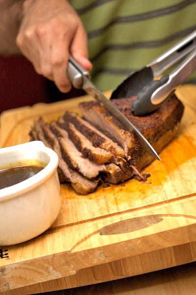 Slicing brisket on a cutting board with gravy boat alongside.