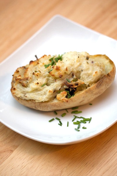 Twice baked potato on a plate with chives.