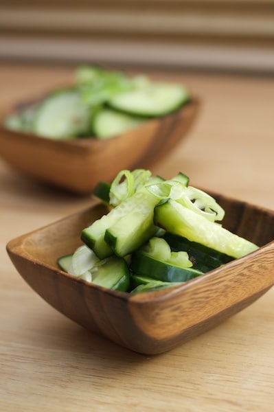 Small bowls of sliced cucumbers and green onions.