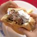 Holding a lamb burger with tzatziki with bites taken out.