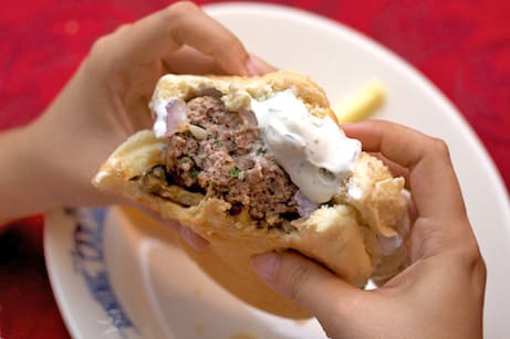 Holding a lamb burger with tzatziki with bites taken out.