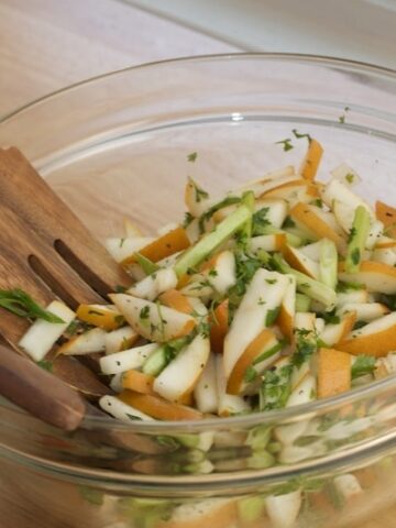 Bowl of Asian pear slaw with serving utensils.