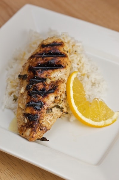 Plate of grilled chicken over rice with an orange slice.