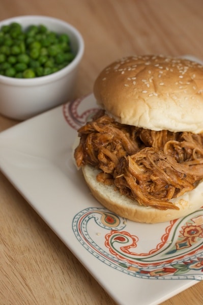 Pulled pork sandwich with a side of peas.