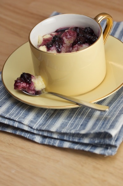 Semolina pudding with blueberry sauce in a cup with a small spoon.