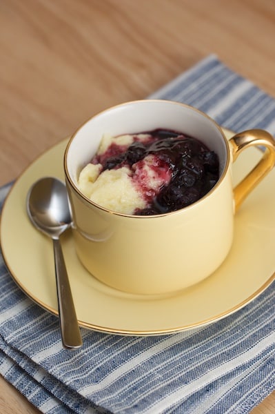 Semolina pudding with blueberry sauce in a cup with a small spoon.