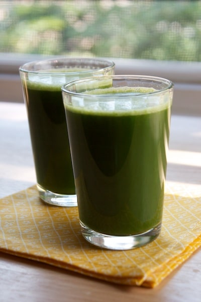 Two glasses of green juice in front of a window.