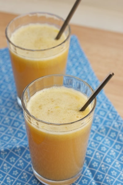 Two glasses of orange, apple, & celery juice with straws.