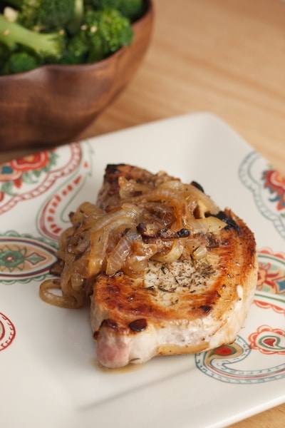 Pork chop on a plate with caramelized onions.