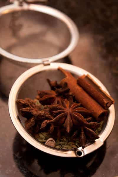 A close-up of a spice ball filled with star anise, cinnamon sticks, and other whole spices.