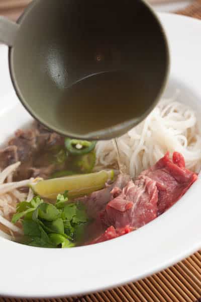 A bowl of pho with broth being poured over top.