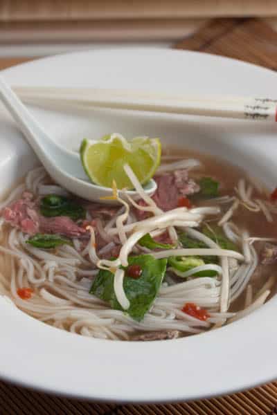 Bowl of beef pho with lime garnish.