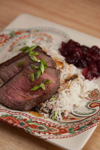 A plate of London broil with rice and cranberry sauce.