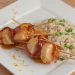 A plate of skewered scallops with bacon and orange zest.