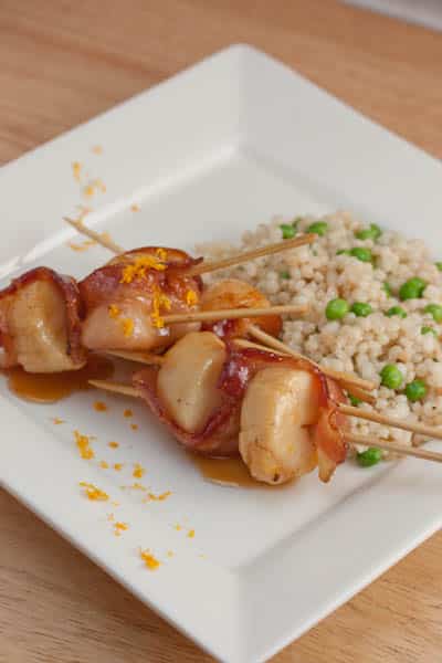 A plate of skewered scallops with bacon and orange zest.