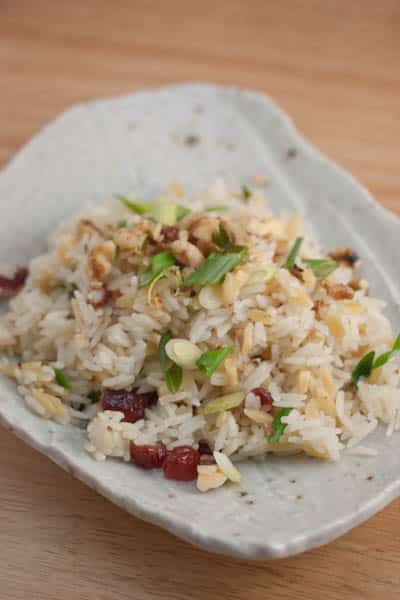 A plate of rice with cranberries, walnuts, and green onions.