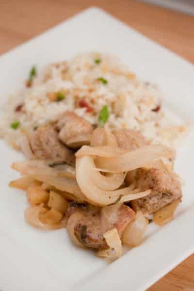 A plate of pork tenderloin with apples and onions served with rice.