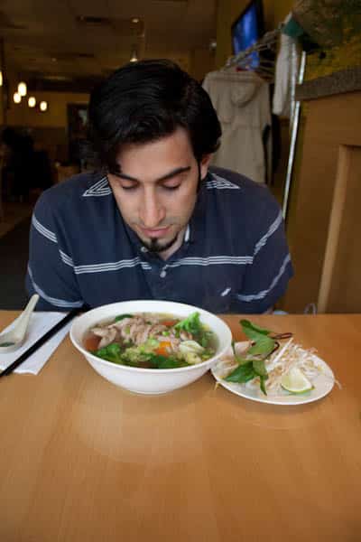 A man sitting at a table with a bowl of pho.