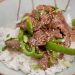 A plate of food steak and green bell peppers over rice.