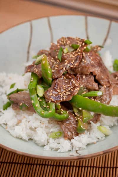 A plate of food steak and green bell peppers over rice.