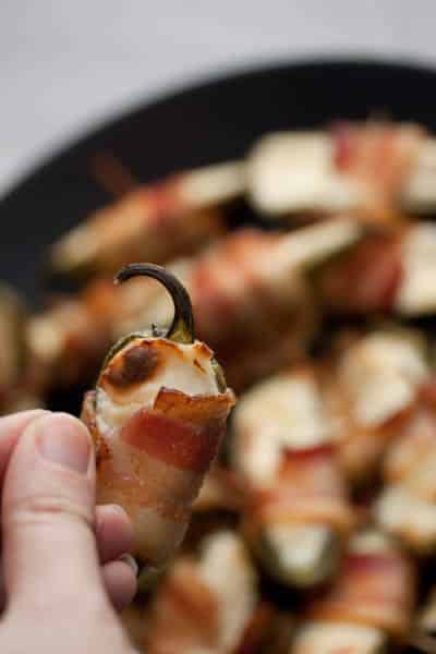 A hand holding a bacon-wrapped jalapeño popper.
