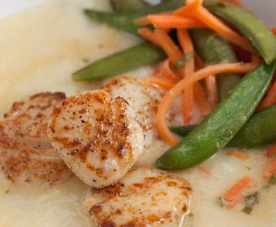 Seared scallops over cauliflower purée with snap peas and carrots alongside.