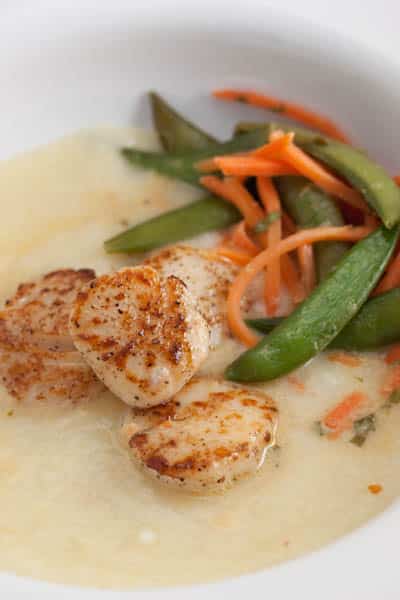 Seared scallops over cauliflower purée with snap peas and carrots alongside.