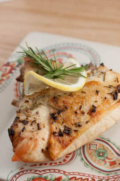 Chicken breast on a plate with lemon and rosemary.