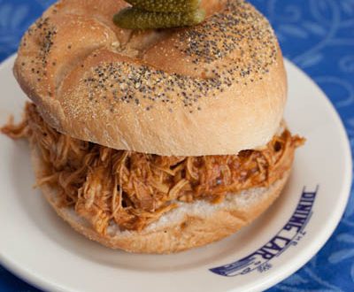 Pulled chicken sandwich with BBQ sauce and pickles on a plate.