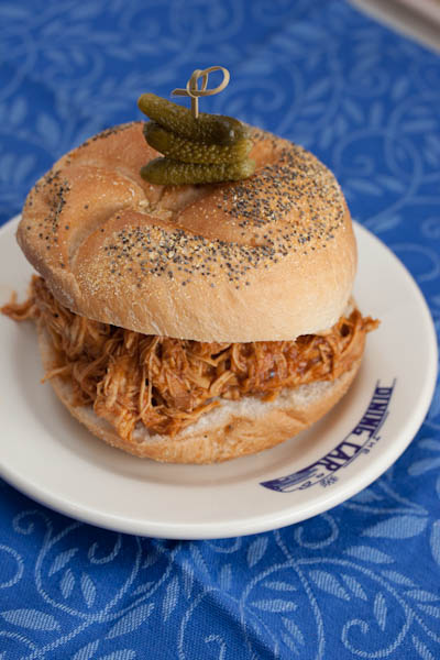 Pulled chicken sandwich with BBQ sauce and pickles on a plate.