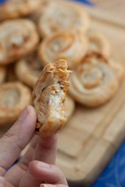 Close-up of a hand holding a swirled cheese crisp with a bite taken out of it.