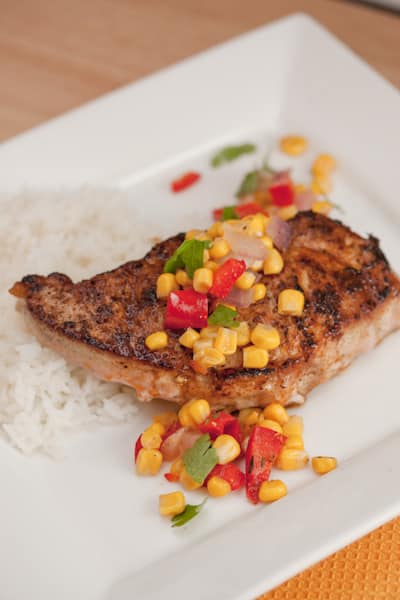 Pork chop with colorful veggies on top served with rice.