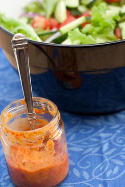 Salad dressing in a jar with a bowl of salad in the background.