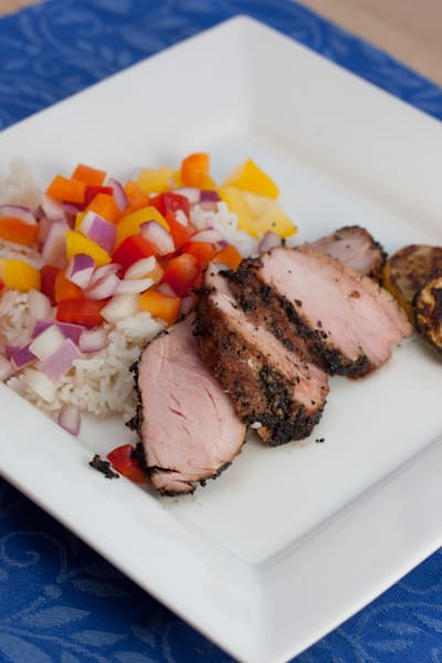 A plate of sliced pork tenderloin with rice and colorful veggies.