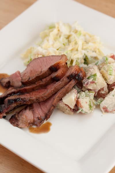 A plate of sliced skirt steak with cole slaw and potato salad.