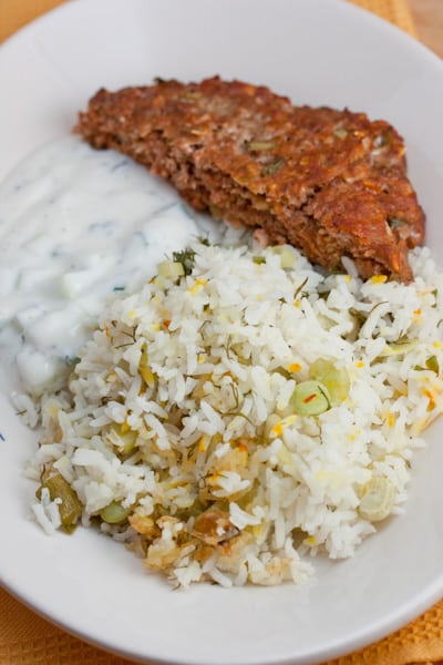 Presian meatloaf on a dish with dill rice and yogurt sauce.